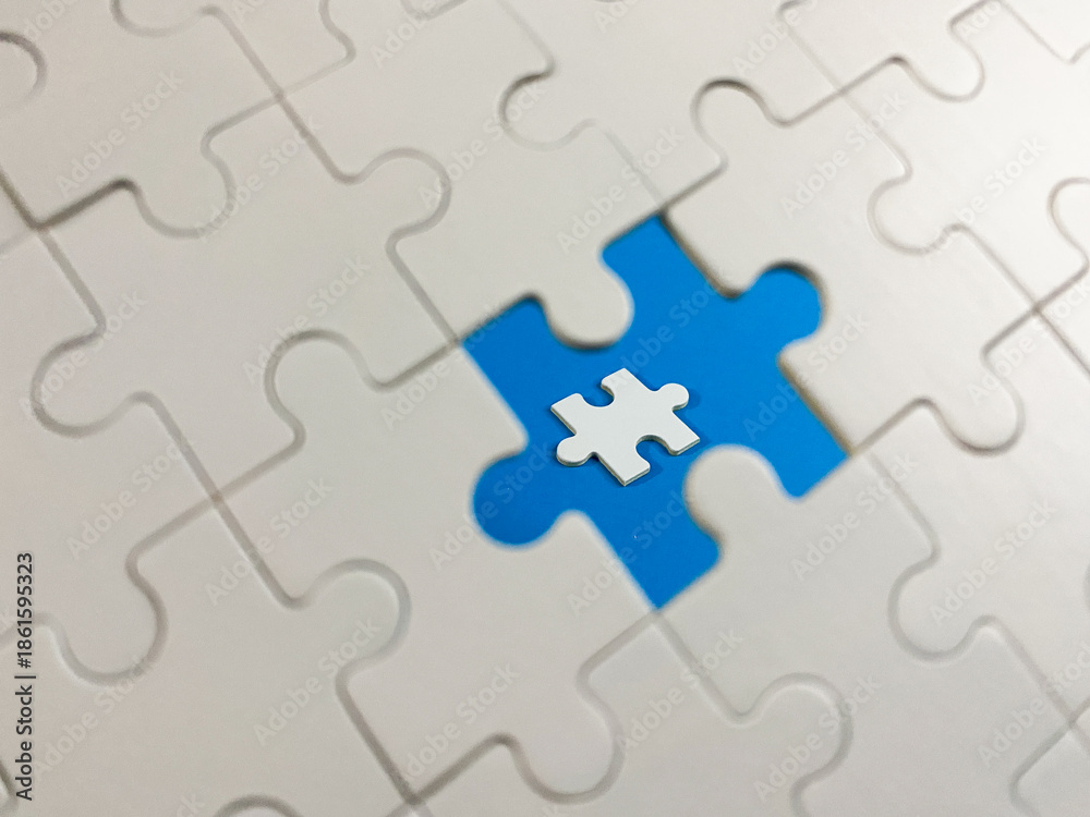 Fototapeta premium A white jigsaw puzzle with one missing piece revealing a vibrant blue background, featuring a tiny miniature piece at the center. Symbolizes problem-solving and innovation.
