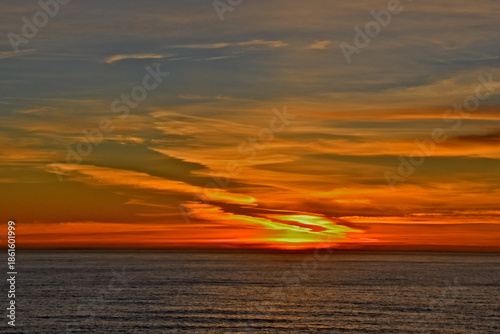 Fiery sunset as sun fall below horizon . Degrading contrails from jets coming in from Hawaii or Asia add diagonal interest 