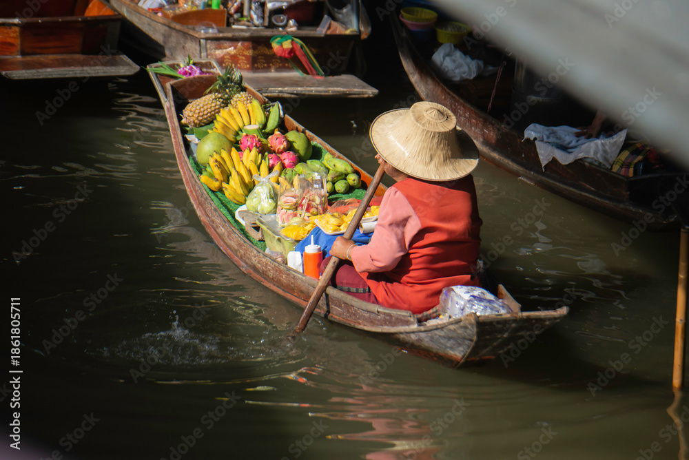 Obraz premium Local fruit vendor rowing a boat at a traditional Thai floating market.
