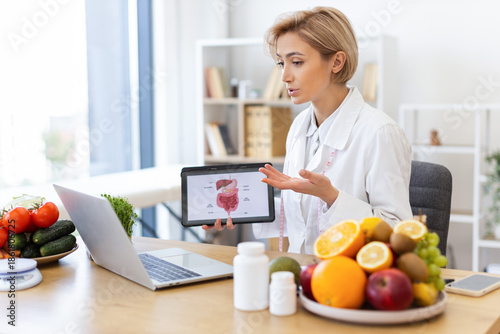A dietitian explains the digestive system to a patient during an online consultation, with healthy food on the table.