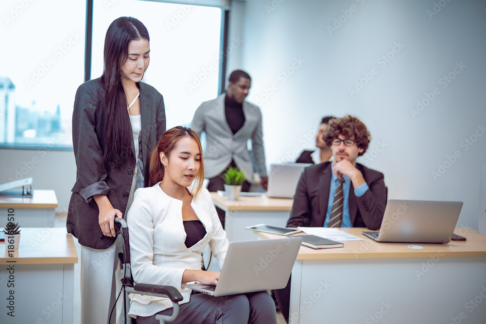 Fototapeta premium Corporate office environment inclusive teamwork with employee using wheelchair working confidently on laptop while teammate observes with supportive promoting diversity equality collaboration.