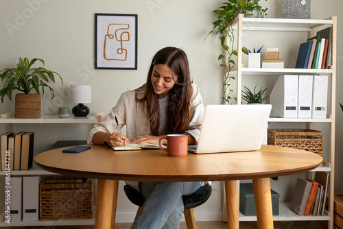 Young happy female caucasian entrepreneur handwriting on a notebook while working at home office