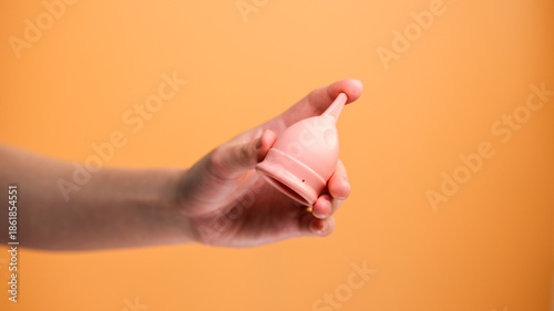 Female Hand Holding Menstrual Cup on Orange Background Minimal Hygiene