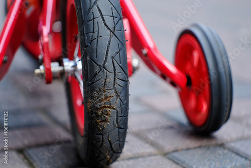 Close up of red bicycle training wheels on paved ground black