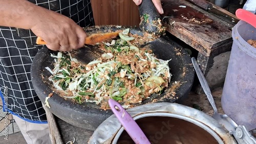 Making Lotek: Indonesian vegetable salad with peanut sauce being mixed in a stone mortar and ready for packaging. Authentic street food preparation process. 
