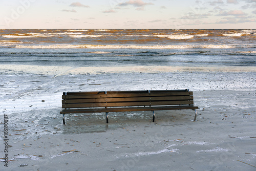 Lonely Wooden Bench on a Sandy Beach with Sea Waves and Clouds