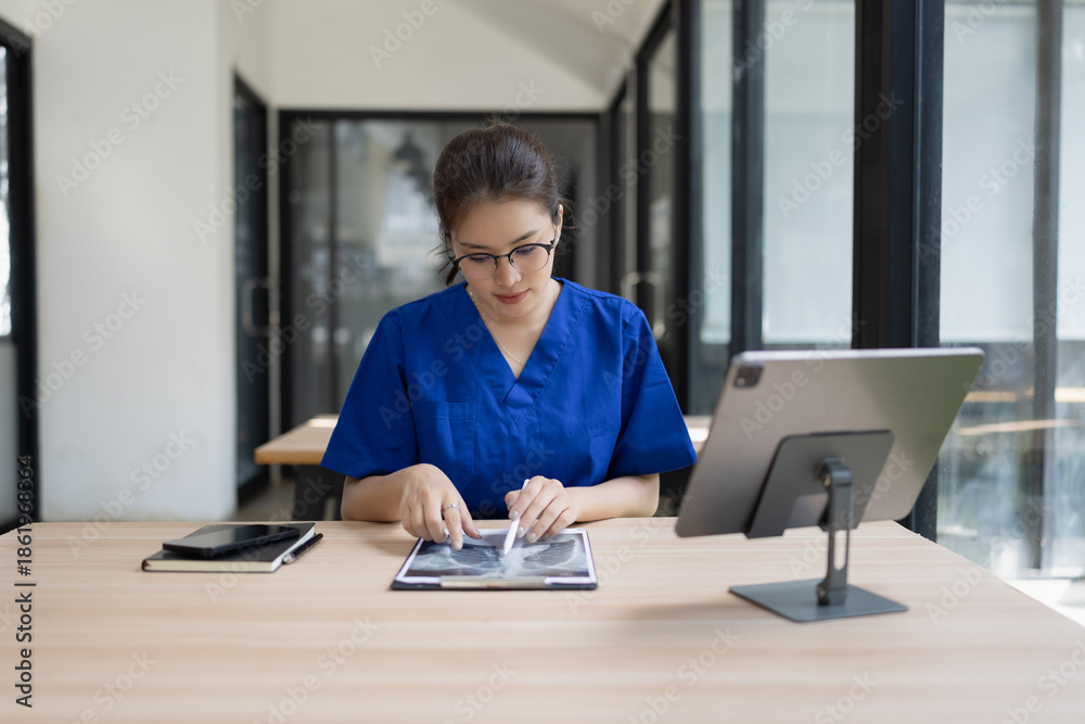 Fototapeta premium Asian female doctor or nurse working and recording information on a clipboard at desk in hospital.