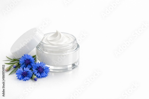 Glass jar of cream with white lid, near blue flowers. Beauty product. Remedy for face or skin around eyes with cornflower extract. Banner with copy space to advertise cosmetics white background