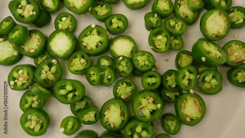 Green Jalapeno peppers slices on plate rotation top view.