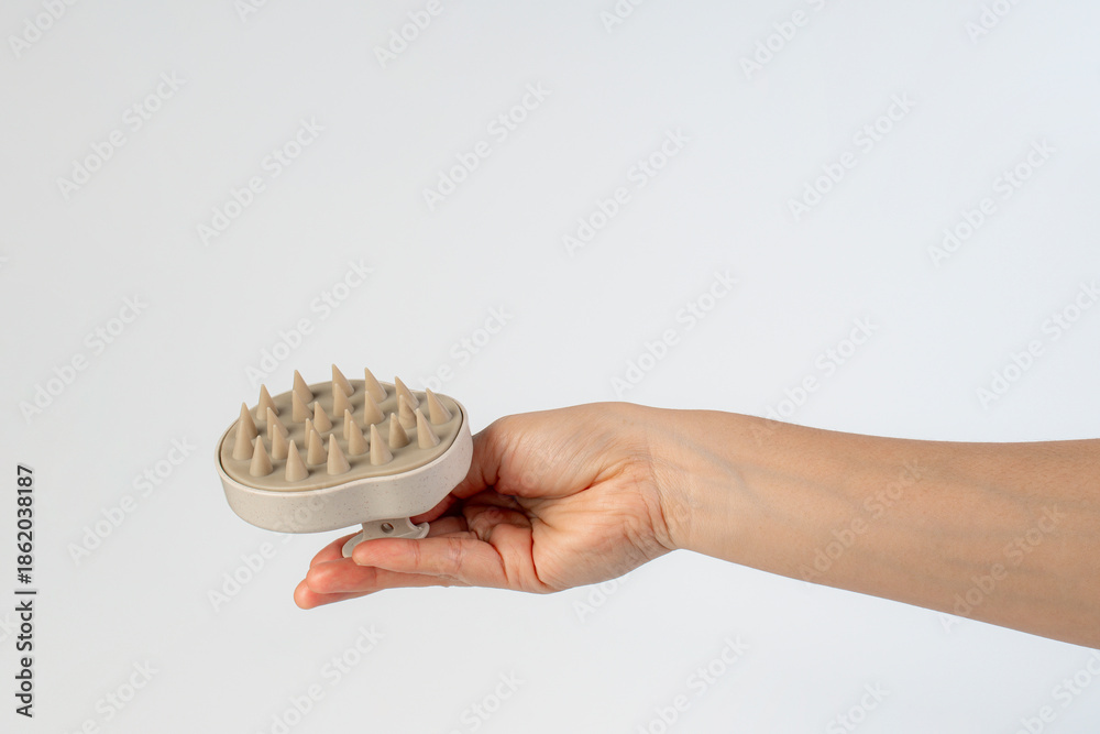 Obraz premium A hair comb used for massaging the scalp while washing hair, held in the hand against a white background.