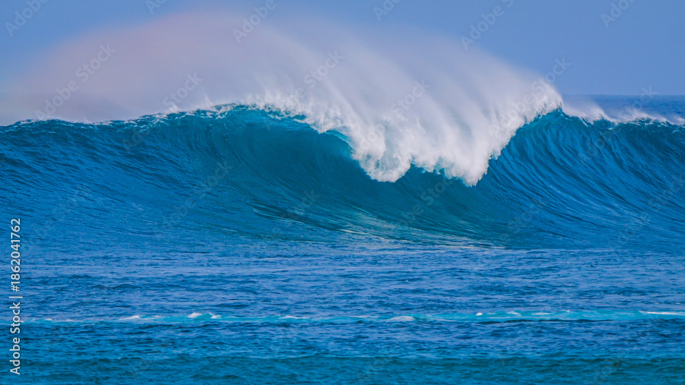 Fototapeta premium CLOSE UP: Perfect glassy blue wave breaks cleanly under offshore wind, sending spray backward in powerful and elegant arc. Smooth texture and energy of the wave highlight raw beauty of Atlantic Ocean