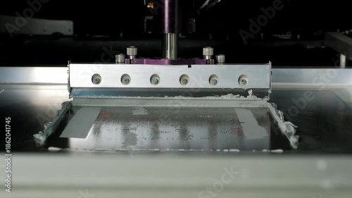 Automated industrial machine applying viscous silver solder paste through a metal stencil onto a printed circuit board for surface-mount technology assembly