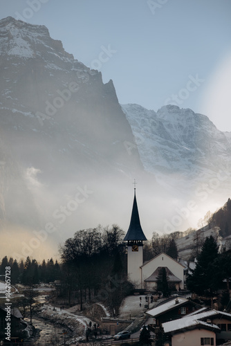 Lauterbrunnen village in winter: a dark and atmospheric mountain scenery. Moody winter landscape of Lauterbrunnen valley with sun rays through the mist.