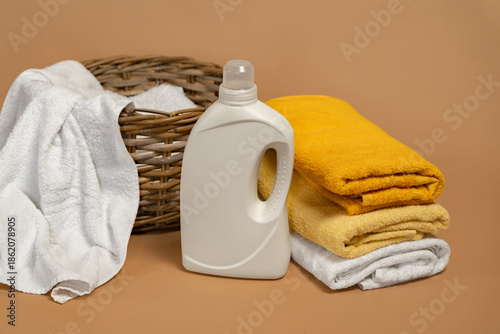 White bottle and freshly washed bath towels with space for advertising design of detergent, washing powder on beige background. Concept of natural fabrics and eco products.