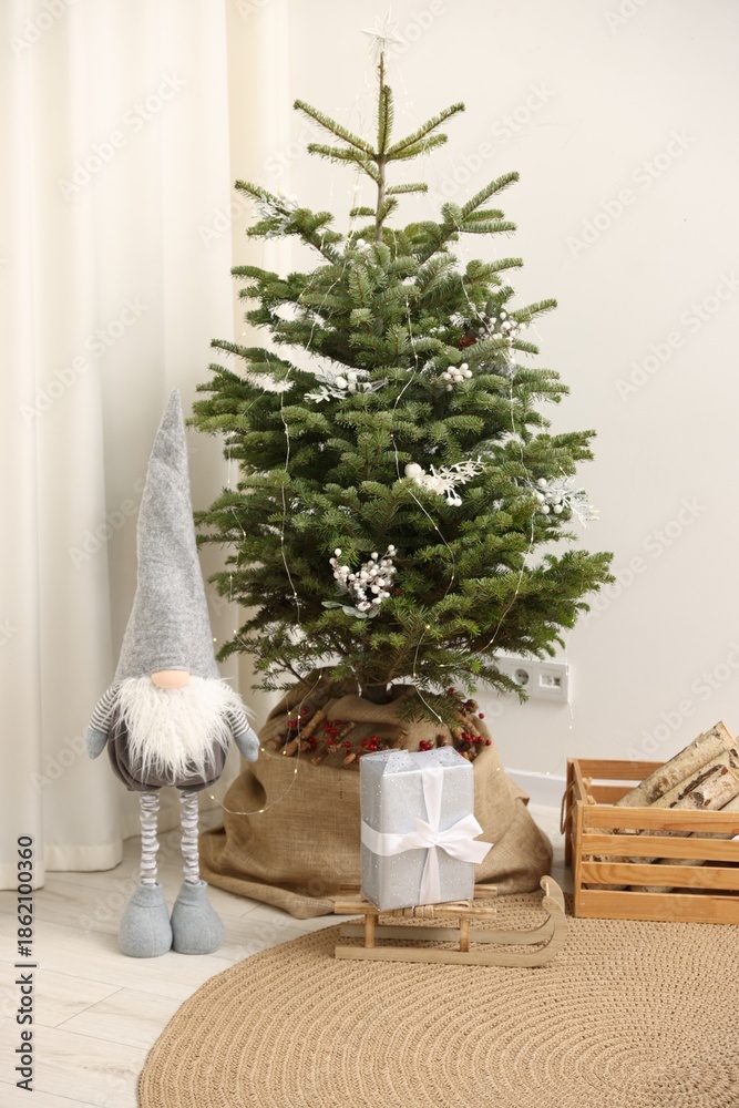 Obraz premium Beautiful Christmas tree, decorative gnome, sledge with gift and firewood at home