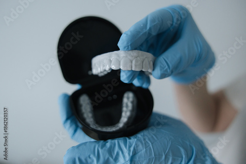 Dental aligner held in blue medical gloves above an open case. Concept of modern dentistry, orthodontic care and oral hygiene.