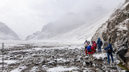 A group of tourists with backpacks are marching along a snowy mountain trail. The view from the back.