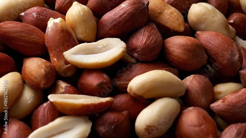 A detailed, macro shot captures a textured assortment of raw shelled peanuts, presenting a mix of light-skinned and red-skinned varieties. The camera slowly glides over the natural composition, highli