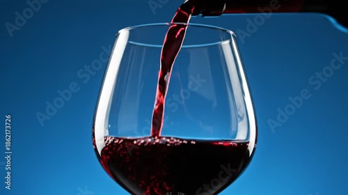 Red wine being poured into a clear wine glass on a vibrant blue background, creating a luxurious atmosphere.