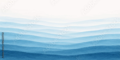 Misty blue sea waves wash onto a sandy beach at dawn with a view of distant mountains and clouds under a soft sunrise horizon