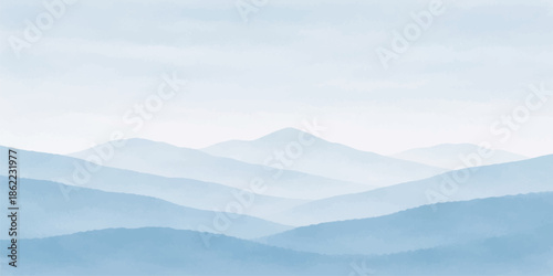 A serene mountain landscape at sunrise features mist and fog rolling through a forested valley as the sun glows over blue hills and snow-capped peaks under a cloudy morning sky