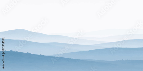 Misty mountain landscape at sunrise with a view of blue hills and forest valleys shrouded in fog and clouds under a hazy morning sky