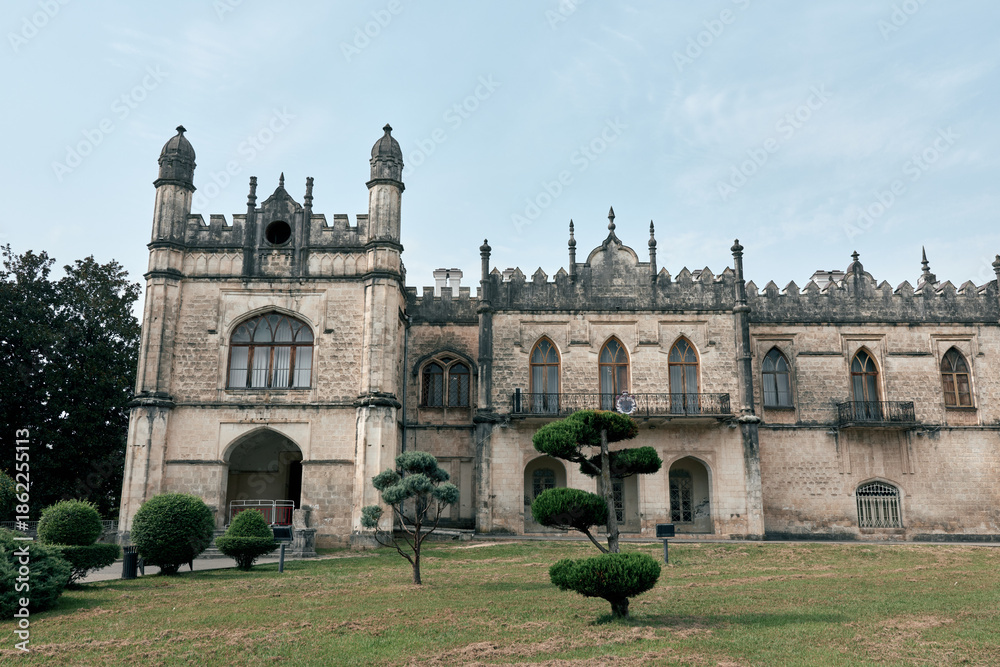 Fototapeta premium historic architecture mansion garden with trimmed topiary and stone facade under overcast sky, authenticity inclusivity
