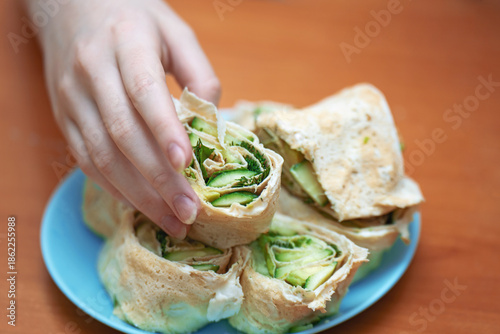 Girl's hand taking a homemade lavash roll with avocado, cucumber, and herbs. Symbol of healthy vegan nutrition