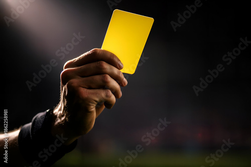 Yellow Card Warning: A stern hand displays a yellow card, a symbol of caution, penalty, or warning, in a setting of high stakes and disciplinary action. 