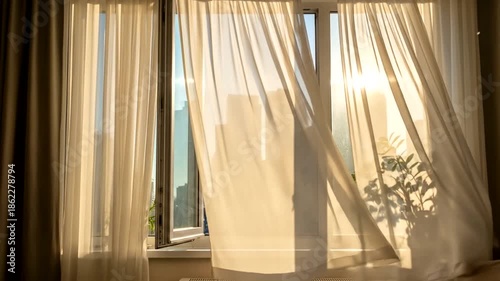 Sunlight streams through an open window with flowing sheer curtains and a green plant.