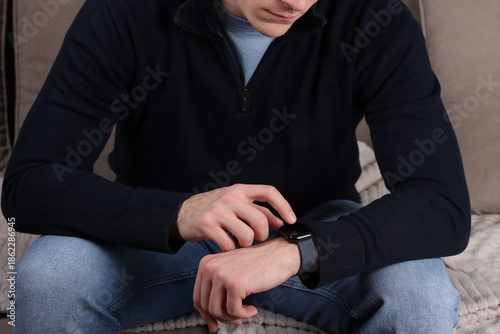 young man sitting on couch and looking and pointing at his smartwatch, wristwatch
