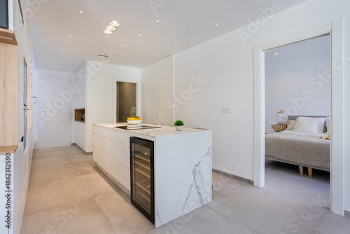 Minimalist marble kitchen island with wine fridge near bedroom entrance in modern interior