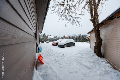 Fotografi Two compact cars sit under fresh snowfall in a yard between cabins