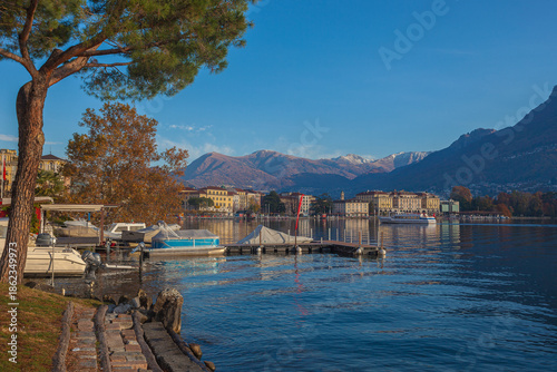Panorama of Lugano lakefront in autumn early morning with mooring for pleasure boats and boat that does tourist service. Lugano, Ticino, Switzerland