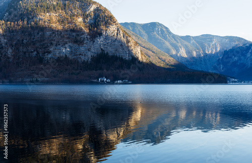 Ruhiger Bergsee mit klarer Spiegelung der umliegenden Berge, sanftes Morgenlicht auf alpiner Landschaft, glatte Wasseroberfläche mit Reflexion und weiter Gebirgskulisse