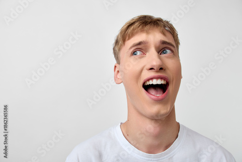 Canvas-taulu Surprised, astonished man looks upward with a wide smile against a clean backgro