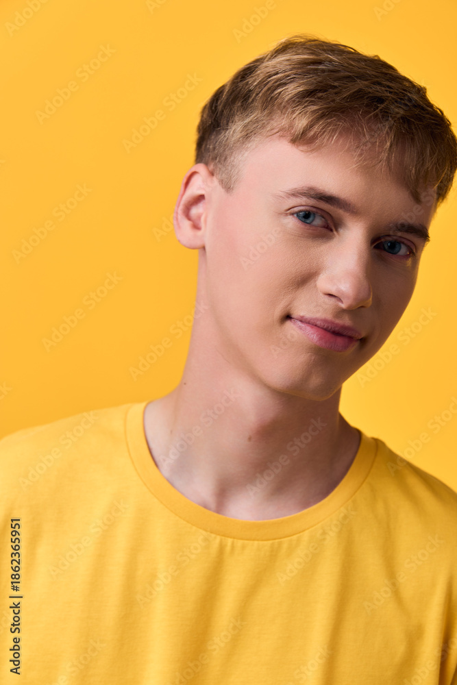 Fototapeta premium Young man in a yellow shirt poses against a vivid yellow backdrop, studio lighting highlighting clean features and a relaxed smile, casual mood perfect for lifestyle and fashion content