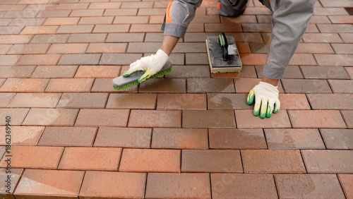 Worker brushing new brick paving during construction
