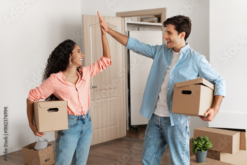 Obraz na plátně Excited young couple gives a high five while celebrating moving day in their new home