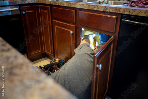Foto handy man fixing plumbing under kitchen sink, tool bag and knowledge of home fixes