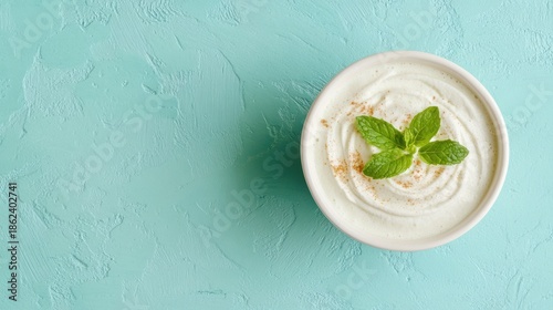 Creamy white yogurt topped with mint leaves and a sprinkle of cinnamon in a white bowl on a teal background