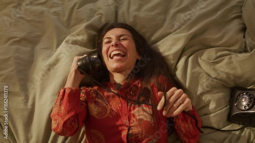Stylish Dreamcore woman falls back talking on retro rotary phone while in bed