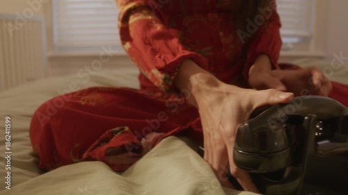 Retro dreamcore woman picks up and plops rotarty phone on bed and starts dialing - close up