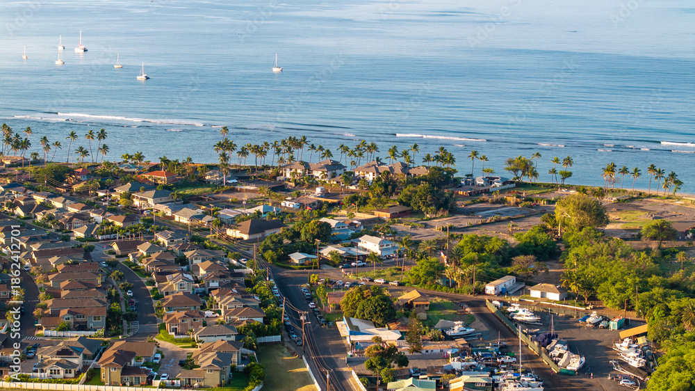 Fototapeta premium Aerial view of Lahaina landscape in Maui, Hawaii wildfire aftermath showing coastline, roads, homes, and sailboats in ocean during morning light