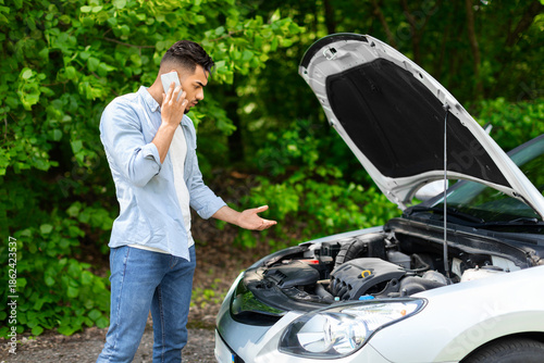 Billede på lærred Confused arab guy driver looking under car hood, calling auto service, upset mid