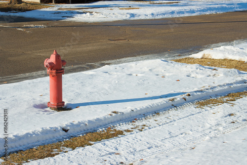 A red fire hydrant in the snow by the street on a sunny winter day