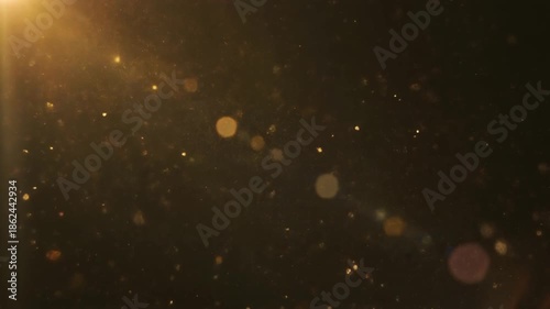 Golden particles floating in dark space with sunlight shining from top left corner