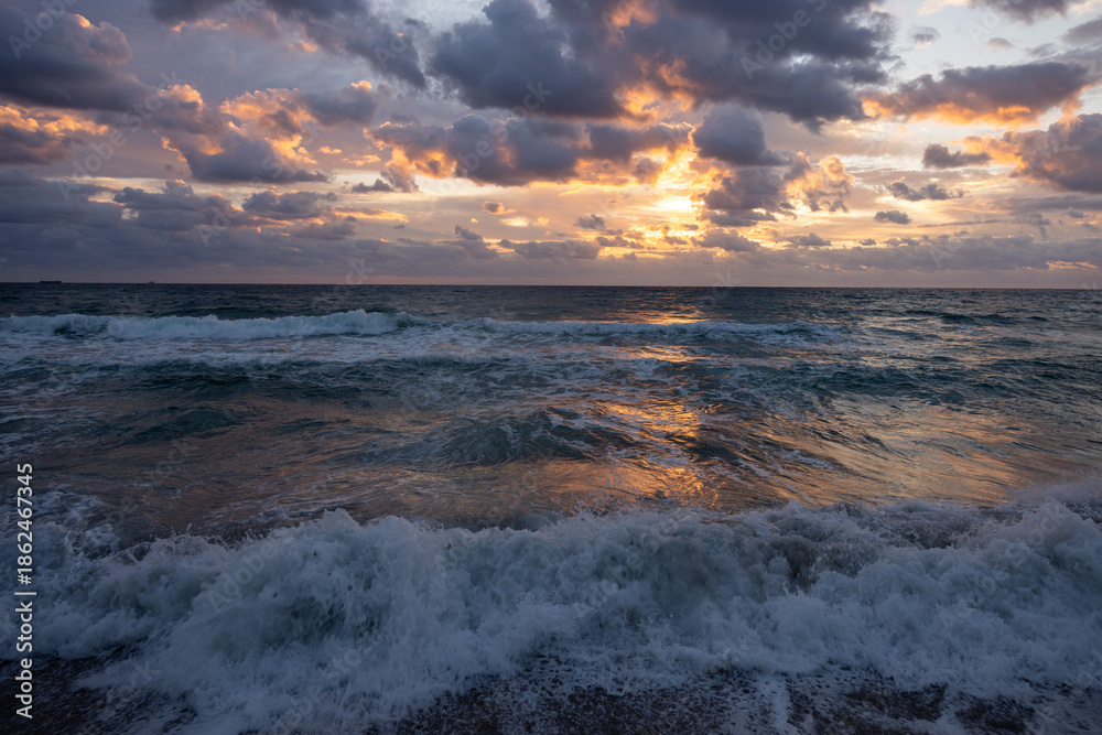 Obraz premium Dramatic sunrise over ocean waves with storm clouds and golden reflections