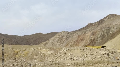 🏗️ Heavy Machinery: Construction Vehicle Working Behind Sand Mountain. A yellow heavy industrial machine cabin moves from left to right behind a sandy mountain ridge. 