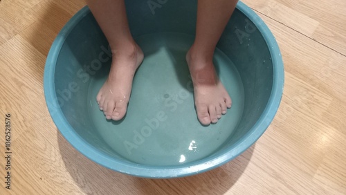 Children’s feet soaking in a basin with warm water at home. Traditional home care routine during cold season. Cozy indoor atmosphere, parental care and comfort concept. Symbol of home remedies